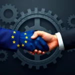 Dłoń w rękawiczce z flagą Unii Europejskiej ściska dłoń w garniturze na tle trybików.